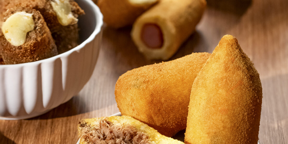 Mão segurando uma coxinha B. foods
